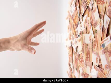 A man's hand reaches for a vertical cash flow of five thousand ruble bills. Stock Photo