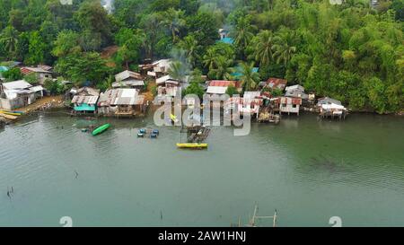 Fishing village with boats and slums with wooden houses, aerial drone. Houses community standing in water in fishing village. Luzon, Philippines. Stock Photo