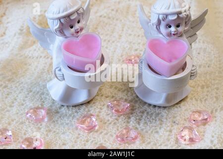 Two white ceramic angel figurines with baskets with pink hearts on a light background. Angel figurine for concept design. The concept of love and kind Stock Photo