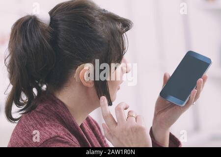 Deaf woman wearing hearing aid and using smartphone Stock Photo