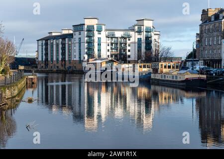 Modern riverside apartment building and moored barges on The Shore reflected in the Water of Leith in Leith, Edinburgh, Scotland, United Kingdom Stock Photo