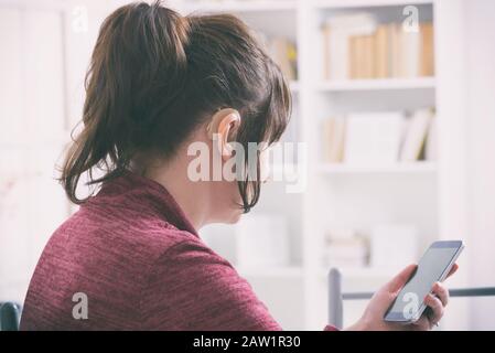 Deaf woman wearing hearing aid and using smartphone Stock Photo
