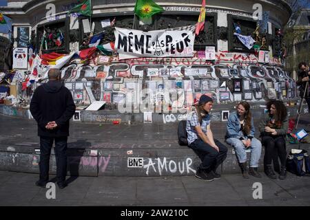 People sitting on steps of Marianne statue in front of messages commemorating victims of Paris and Brussels attacks, Place de la République, Paris, France - April 2016 Stock Photo