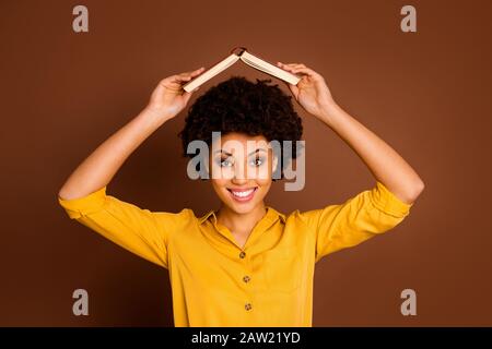 I'm home. Closeup photo of pretty funny dark skin lady hold open book homework under head fooling around childish mood wear yellow shirt isolated Stock Photo