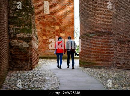 Two People Walk Between Large Brick Walls To An Opening Stock Photo