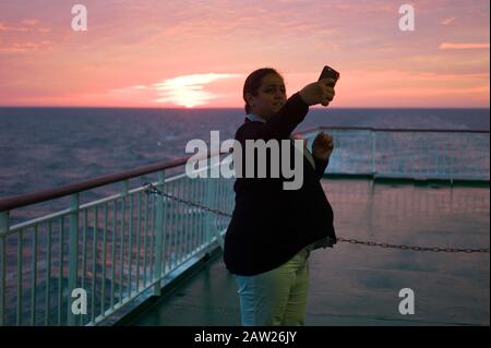 Woman taking selfie against sunset on a cross-channel ferry Stock Photo