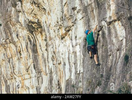 Man with a rope engaged in the sports of rock climbing on the rock. Stock Photo