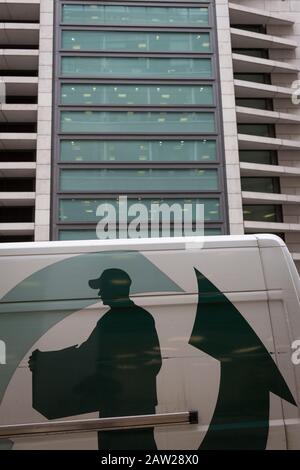 The graphic showing a person delivering a package, on the side of a courier's van, passing beneath corporate offices in the City of London, the capital's financial district, on 4th February 2020, in London, England. A man wearing a peaked cap is shown carrying a box with a large arrow pointing upwards to nearby offices. Stock Photo