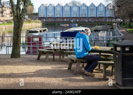 A middle aged man sitting on a park bench having a coffee next to a river Stock Photo