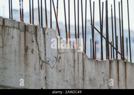 A dilapidated gray concrete wall with rusty rebar protruding from the top of it against a blurred background of an apartment building Stock Photo