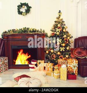Colorful Christmas fir-tree, golden christmas decorations and gifts near fireplace in interior. New year. Christmas. Stock Photo