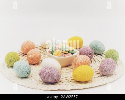 Round placemat topped with Easter eggs covered in sparkly string and a white bowl of pastel colored white chocolate mint candies. Stock Photo