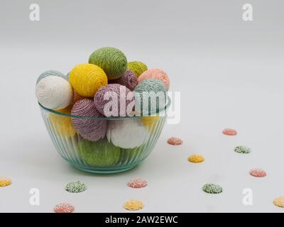 Colorful Easter eggs in a bowl and pastel colored candies surrounding it on a white background. Stock Photo