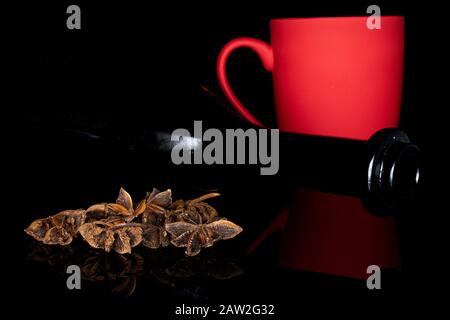 Lot of whole aromatic brown badian with red ceramic cup and brown glass bottle isolated on black glass Stock Photo