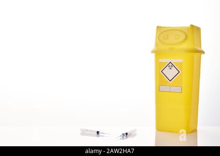 A large yellow sharpsbin container on the right, with two syringes with needles front centre with copy space centre and to the left. Stock Photo