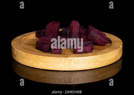 Lot of pieces of raw sweet beetroot on round bamboo coaster isolated on black glass Stock Photo