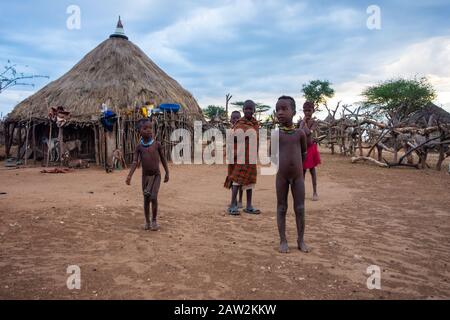 Turmi, Ethiopia - Nov 2018: Hamer tribe kids wrapped into colorful blankets in front of their family hut. Omo valley Stock Photo
