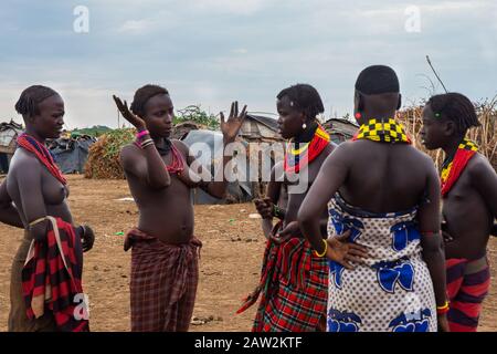 Omorate, Ethiopia - Nov 2018: Young men and women wearing traditional tribal clothes and necklaces talking with each other. Omo valley Stock Photo