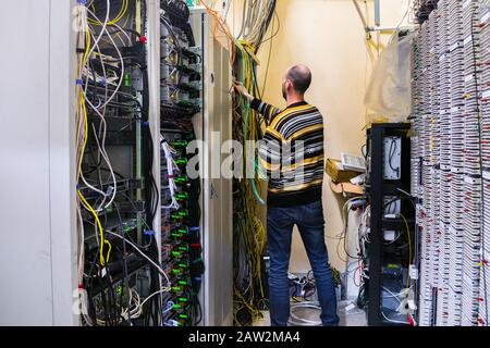 The man is working in the server room of the data center. The engineer connects the wires to provide Internet communication. The system administrator Stock Photo