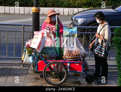 A woman customer wearing a mask buys food from a street food seller who is also wearing a mask in central Bangkok, Thailand, Asia. The seller's 'shop' is a mobile cart on the pavement. The wearing of masks in Bangkok has increased in the light of concerns about the novel coronavirus (2019-nCoV) that was first reported from Wuhan, China, on 31 December 2019. Stock Photo