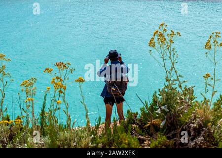 A young man is standing on the coast and watching at horizontal line of the sea using binoculars. Stock Photo