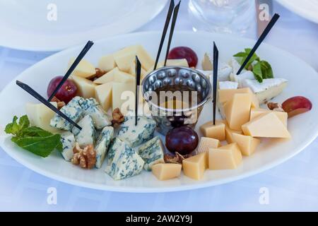 A dish with three kinds of cheese, grapes, walnuts, and honey standing on the white table. Stock Photo