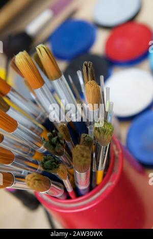 Paint brushes in a pot with different coloured paints in the background Stock Photo