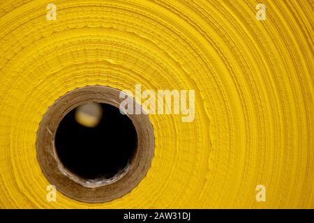 Close-up of the end of a large roll of yellow plastic polythene sheet on a roll with a large cardboard tube through the middle for packaging Stock Photo