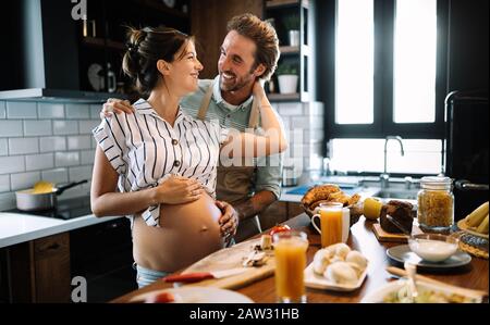 Beautiful young couple is talking and smiling while cooking healthy food in kitchen at home Stock Photo