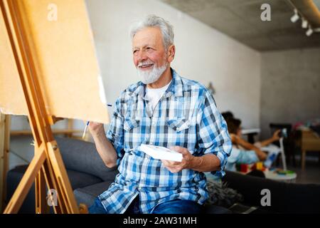 Handsome mature man artist paints on canvas painting on the easel Stock Photo