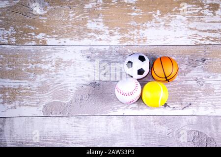 A closeup image of a stack of sports balls against a reflective blue background. In the stack is a football, baseball, basketball and tennis ball. Stock Photo