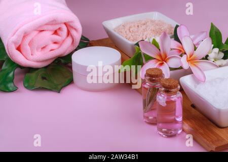 Spa composition with bowls with rock white and pink salt and flowers, towel, cream and lotion on pinkk background. Body scrub and massage treatment Stock Photo