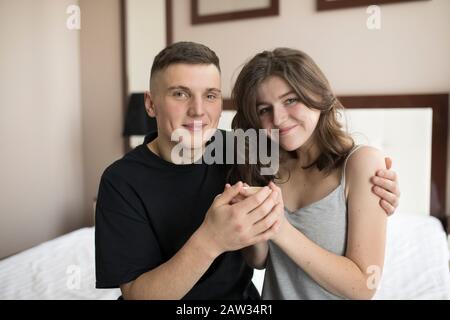 Smiling young man embracing girlfriend and looking at camera. Stock Photo