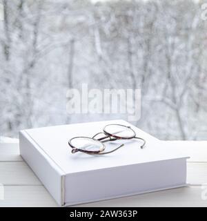 Round vintage reading glasses lie on a white thick notepad against the backdrop of the forest Stock Photo
