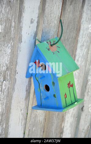 Little blue and green birdhouse hanging on wooden fence Stock Photo