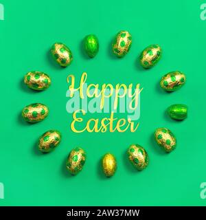 Chocolate easter eggs in gold and green foil in round with the sign Happy Easter in the middle on green background. Easter concept, square Stock Photo