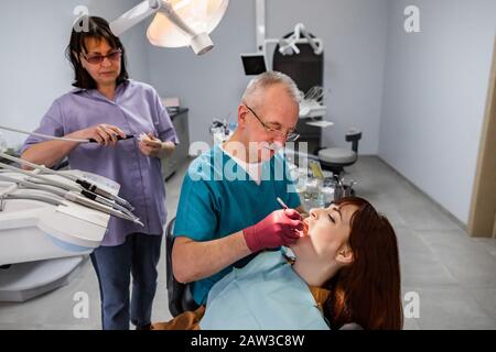 Dentist team, elderly man and woman, and young female patient having professional treatment in modern dental office Stock Photo