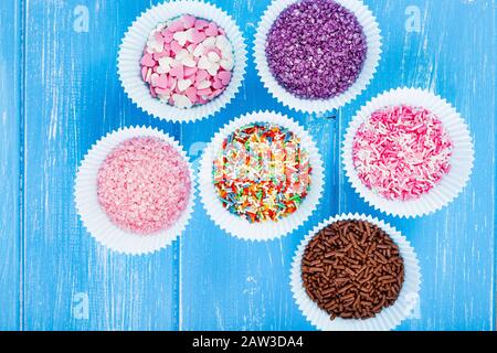 Colorful candy sprinkles on the paper cupcake holder. Blue wooden rustic background. Stock Photo