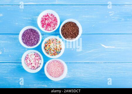 Colorful candy sprinkles on the paper cupcake holder. Blue wooden rustic background. Stock Photo