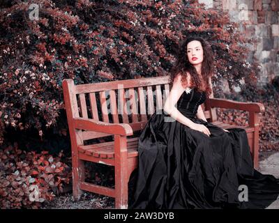 Beautiful elegant woman wearing black dress and sitting on a bench Stock Photo