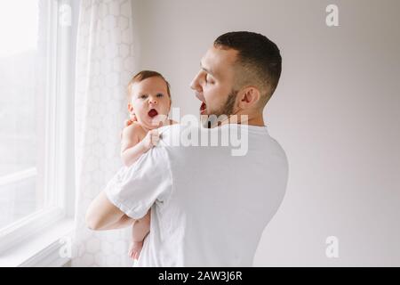 Happy Caucasian father holding newborn baby. Male bearded man parent imitating his yawning child daughter son. Authentic lifestyle candid funny moment Stock Photo