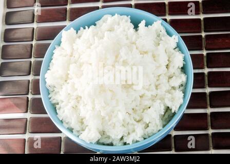 cooked white rice in a blue ceramic bowl. The background is a dark bamboo place mat. Shot indoors in natural day light. Stock Photo