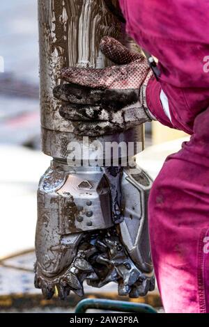 worker guides drill bit into drill hole on drill floor Stock Photo