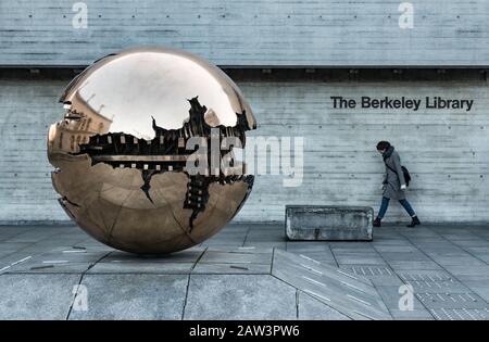 Dublin, Ireland - 29th January 2020:  Student walking by the golden globe sculpture Sphere at Trinity College. Stock Photo