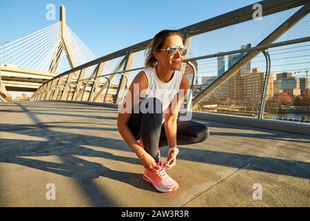 An athletic woman ties her shoe in front of the Zakim Bridge in Boston Stock Photo