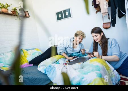 Woman showing mobile phone to friend while leaning on bed at home Stock Photo
