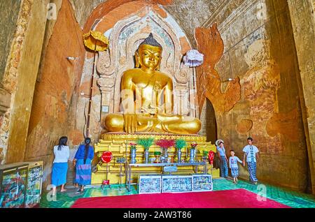 BAGAN, MYANMAR - FEBRUARY 25, 2018:  The Htilominlo Temple prayer hall with amazing golden image of Buddha, surrounded by ancient frescoes and molding Stock Photo
