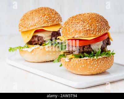 Two hamburgers on white board on white background, hot homemade unhealthy fat food Stock Photo