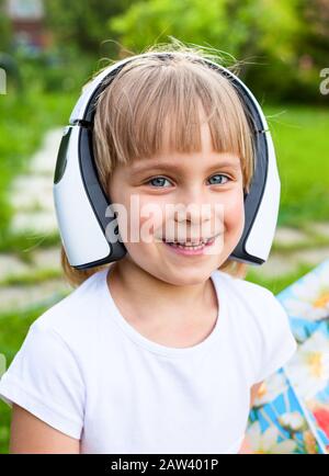 Portrait of cute 5 years girl wearing wireless headphones outdoors Stock Photo