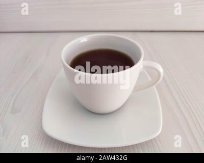 A white cup of tea or coffee and saucer on the wooden table with copy space. A photo for a café or restaurant menu or package backdrop. Stock Photo